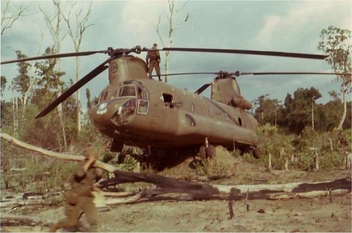 The Aircraft Commander (AC), Captain Larry D. Mohler, is on top of CH-47B 66-19114 making a final inspection before flying the damaged aircraft, alone, off to the side of the LZ.