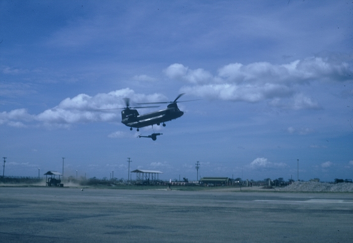 An unknown CH-47A Chinook helicopter lifts a howitzer at Soc Trang in the Republic of Vietnam, date unknown.